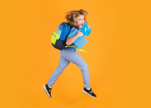 Volle Länge des aufgeregten Springens. Lustiges Schulkonzept. Kleiner Junge mit Rucksack geht zur Schule und springt. Schulkind, Schüler springen auf gelbem Hintergrund - Foto, Bild