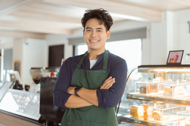 Young Asian male barista in apron having arms folded and smiling while looking at camera with copy space - Φωτογραφία, εικόνα