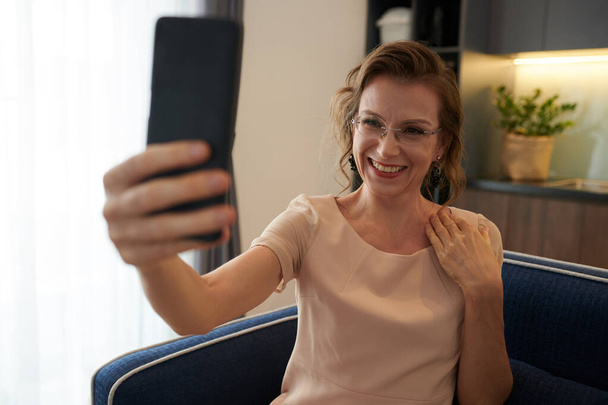 Ευτυχισμένη μεσήλικη γυναίκα με γυαλιά που βγάζει selfie στο smartphone - Φωτογραφία, εικόνα