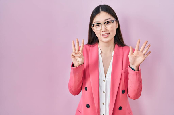 Čínský obchod mladá žena nosí brýle ukazující a ukazující nahoru s prsty číslo osm při úsměvu sebevědomě a šťastně.  - Fotografie, Obrázek