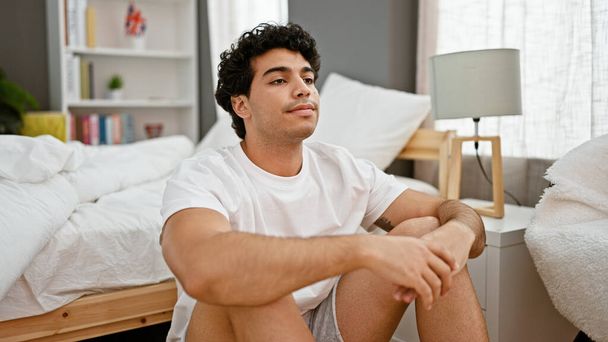 Giovane uomo latino seduto sul pavimento pensando a camera da letto - Foto, immagini
