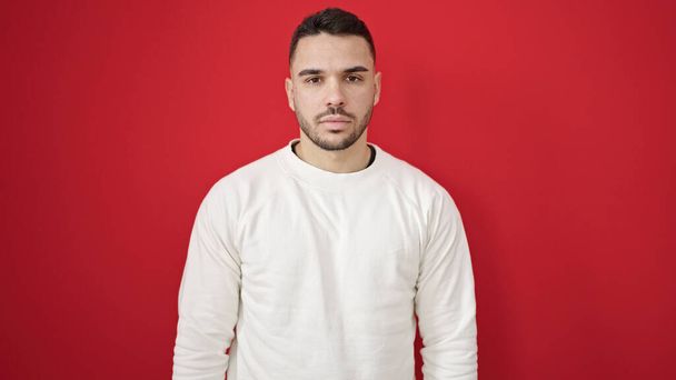 Молодой латиноамериканец с серьезным выражением лица на изолированном красном фоне - Фото, изображение