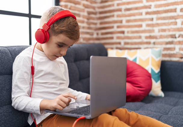 Чарівний іспаномовний хлопчик використовує ноутбук і навушники, що сидять на дивані вдома
 - Фото, зображення