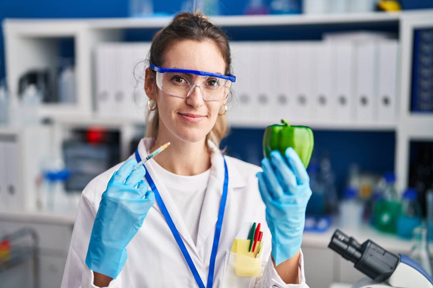 Mujer hispana joven que trabaja en el laboratorio científico con vegetales relajados con expresión seria en la cara. simple y natural mirando a la cámara.  - Foto, Imagen
