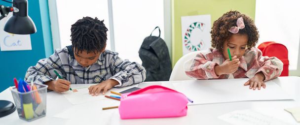 Uroczy afrykański chłopiec i dziewczęta studenci siedzi na stole rysunek na notatniku w klasie - Zdjęcie, obraz