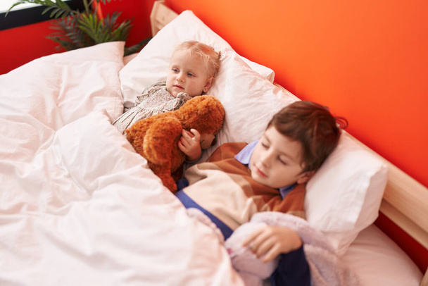 Adorable garçon et fille étreignant ours en peluche dormant sur le lit dans la chambre - Photo, image