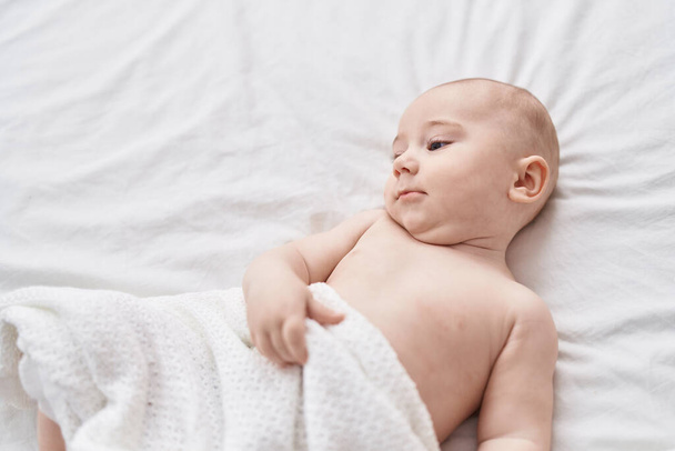 Adorable caucasian baby lying on bed at bedroom - Fotó, kép