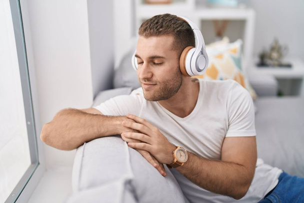 Joven hombre caucásico escuchando música sentado en el sofá en casa - Foto, Imagen