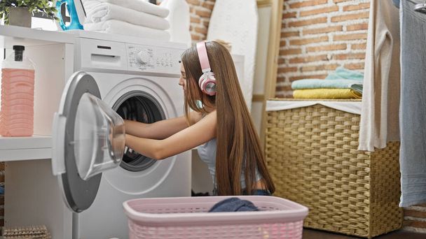 jong mooi meisje wassen kleding luisteren naar muziek in wasruimte - Foto, afbeelding
