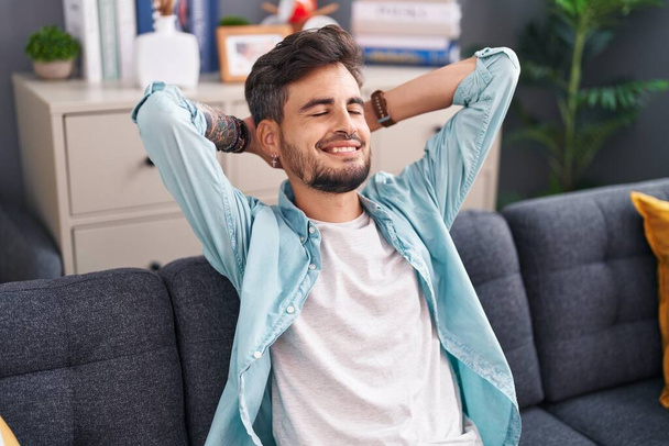 Fiatal spanyol férfi nyugodt kezekkel a fején ül otthon a kanapén. - Fotó, kép