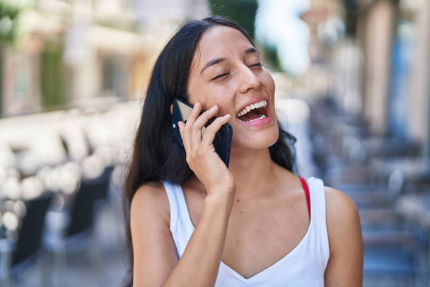 Mladý krásný hispánský žena usměvavý sebevědomý mluvení na smartphone na ulici - Fotografie, Obrázek