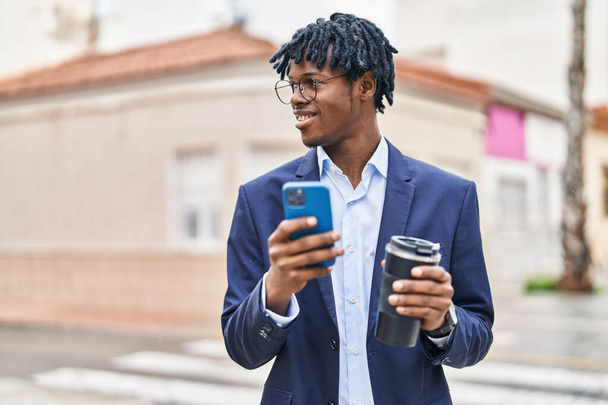 African american man executive using smartphone drinking coffee at street - Photo, Image