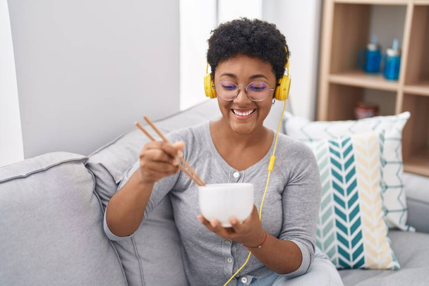 Mujer afroamericana escuchando música comiendo comida china en casa - Foto, imagen