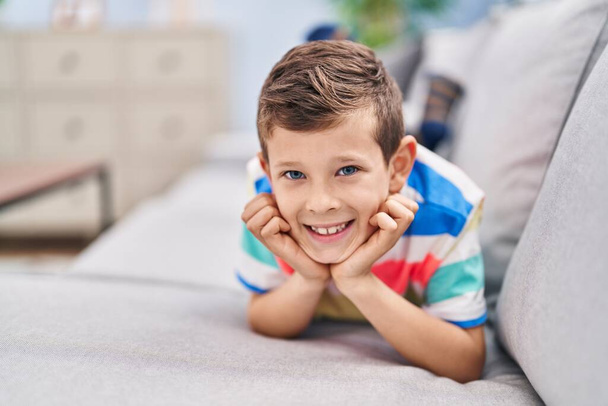 Criança loira sorrindo lyig confiante no sofá em casa - Foto, Imagem