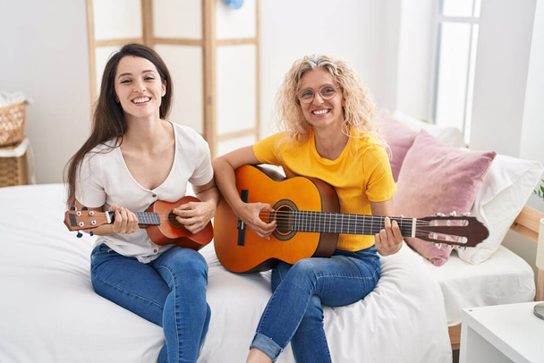 Дві жінки мати і дочка грають на класичній гітарі і укулеле в спальні
 - Фото, зображення