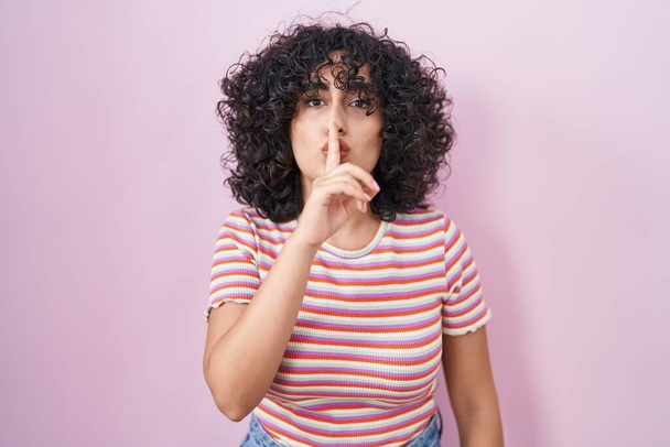 Jovem mulher do Oriente Médio em pé sobre fundo rosa pedindo para ficar quieto com o dedo nos lábios. silêncio e conceito secreto.  - Foto, Imagem