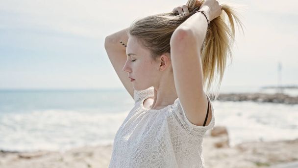 Kumsalda saçlarına dokunan sarışın genç bir kadın. - Fotoğraf, Görsel