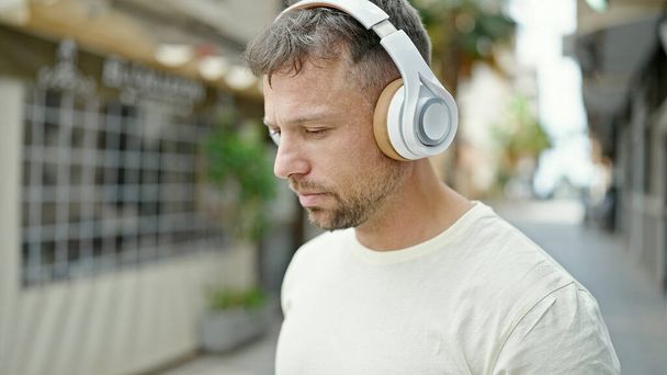 Junger Mann hört Musik mit entspanntem Gesichtsausdruck auf der Straße - Foto, Bild