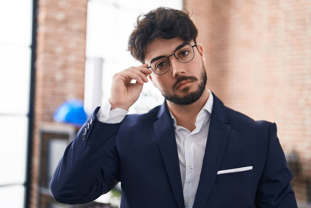 Fiatal spanyol férfi üzletember áll komoly arckifejezéssel az irodában - Fotó, kép