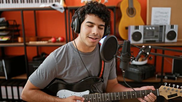 Молодой латинский музыкант поет песню, играя на электрогитаре в музыкальной студии - Фото, изображение