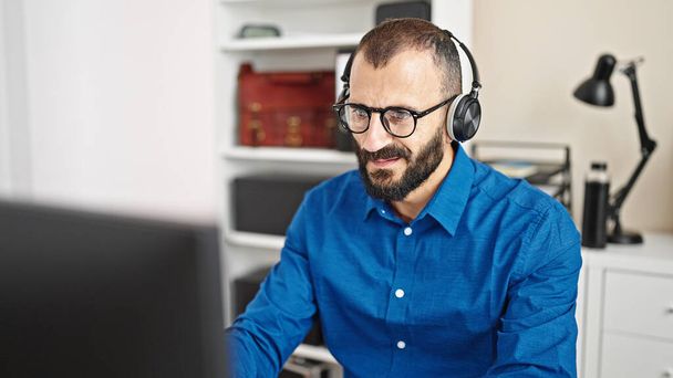 Молодий іспаномовний чоловік бізнесмен використовує комп'ютер і навушники в офісі - Фото, зображення