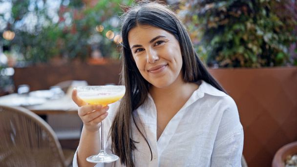 Young beautiful hispanic woman drinking a tropical cocktail drink at bar terrace - Photo, Image