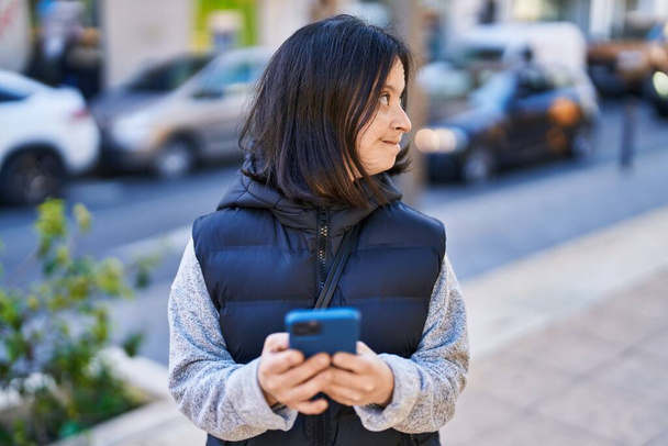 Młoda kobieta z zespołem Downa uśmiecha się pewnie za pomocą smartfona na ulicy - Zdjęcie, obraz