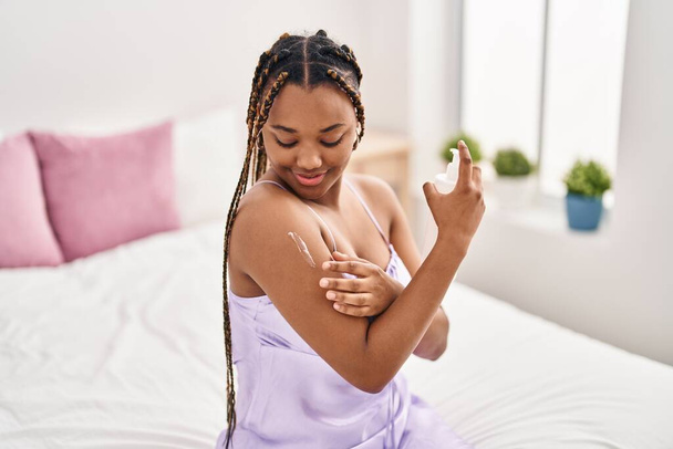 Африканская американка применяет лечение кожи сидя на кровати в спальне - Фото, изображение