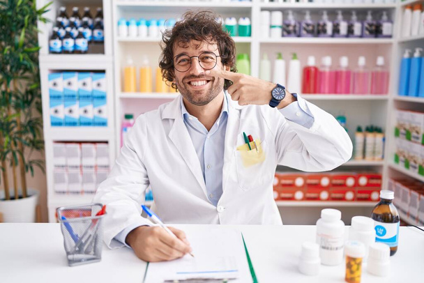 Латиноамериканец, работающий в аптеке, тычет пальцем в лицо и нос, весело улыбаясь. концепция красоты  - Фото, изображение