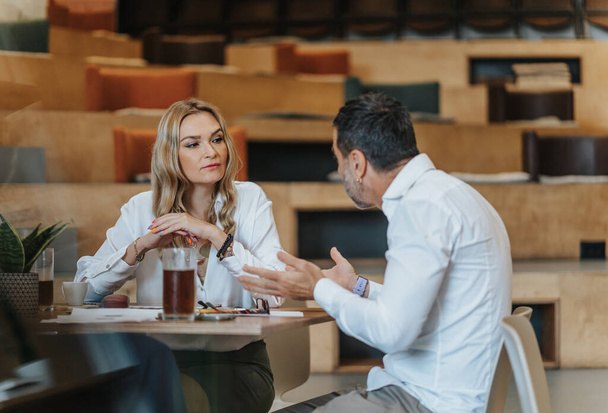 Portret van een bebaarde zakenman die naar een jonge vrouw luistert tijdens een ontmoeting met documenten - Foto, afbeelding