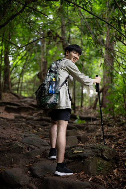 A portrait of a handsome and happy Asian male hiker with a backpack and trekking gear climbing up the stones, exploring the forest, and enjoying his hiking trip. - Foto, Bild