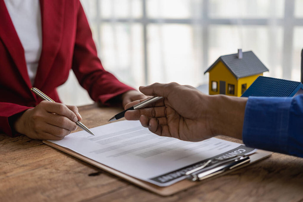 The real estate agent discusses the terms of the home purchase agreement and asks the client to sign paperwork to contract and deliver the home. - Foto, afbeelding