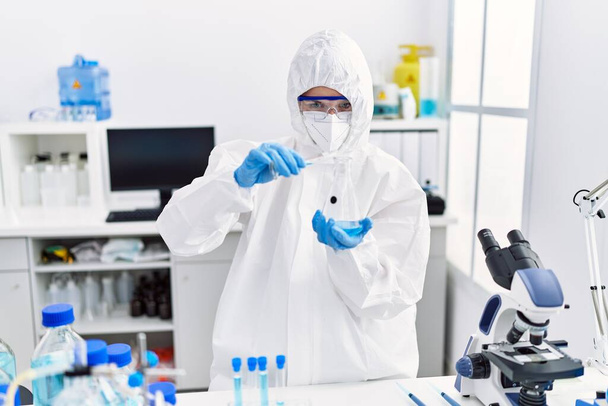 Junge blonde Wissenschaftlerin in Sicherheitsuniform gießt im Labor Flüssigkeit auf Reagenzglas - Foto, Bild
