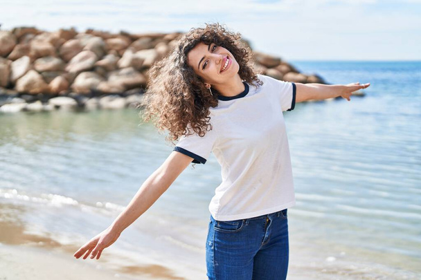 Giovane donna ispanica sorridente fiducioso in piedi con le braccia aperte al mare - Foto, immagini