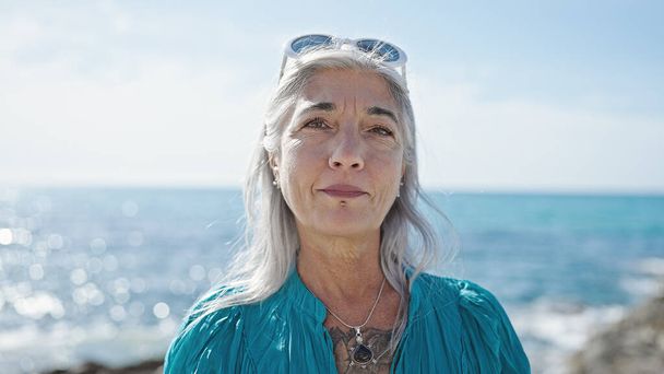 海辺でリラックスした表情で立っている中年の灰色の女性 - 写真・画像