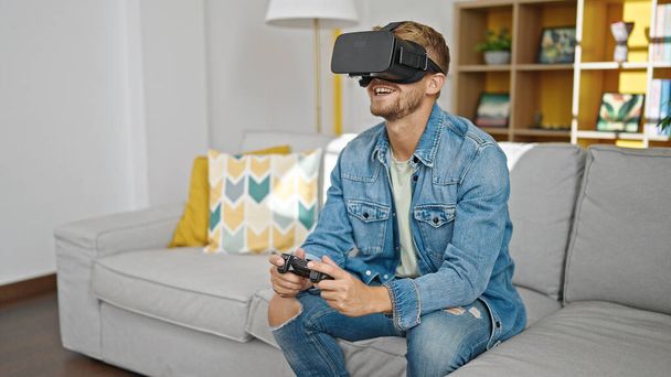 Jeune homme caucasien jouer à un jeu vidéo en utilisant des lunettes de réalité virtuelle et joystick à la maison - Photo, image