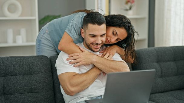 Kadın ve erkek dizüstü bilgisayar kullanıyor. Evde birbirlerine sarılıyorlar. - Fotoğraf, Görsel