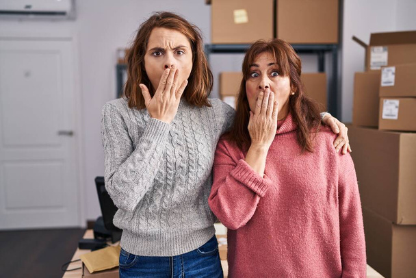 Dwie kobiety pracujące w małym biznesie, zakrywające usta ręką, zszokowane i bojące się pomyłki. zaskoczona ekspresja  - Zdjęcie, obraz