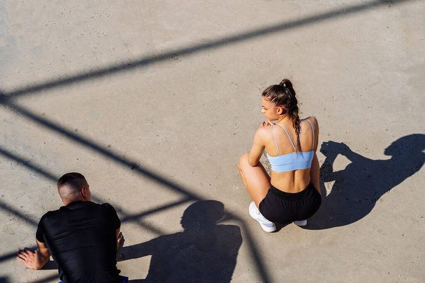 Een mooi fit meisje hurkt en praat met haar vriend terwijl hij push-ups doet - Foto, afbeelding