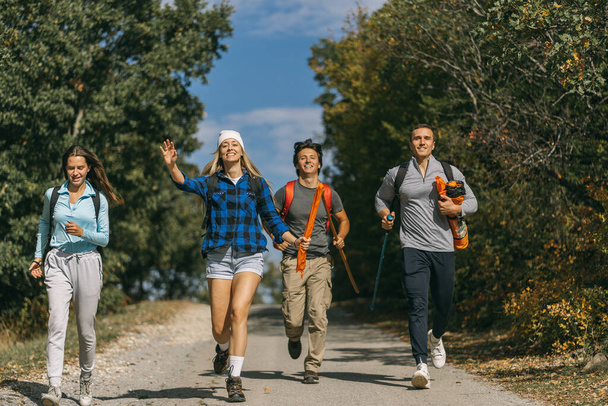 Jóvenes hombres y mujeres excursionistas corriendo por la calle entre las montañas que estaban haciendo senderismo - Foto, Imagen