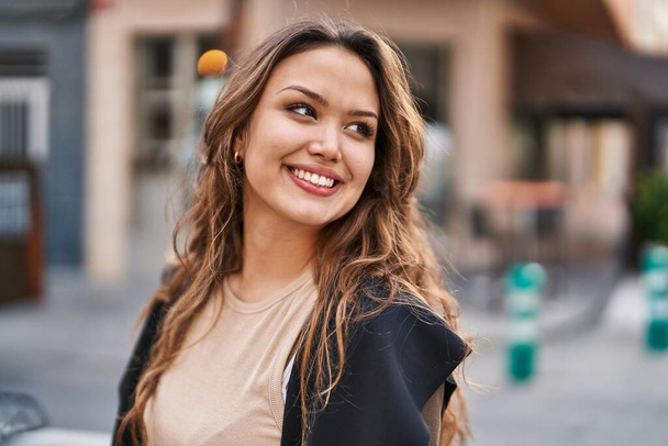 Молода красива іспаномовна жінка посміхається впевнено дивлячись в бік на вулиці
 - Фото, зображення