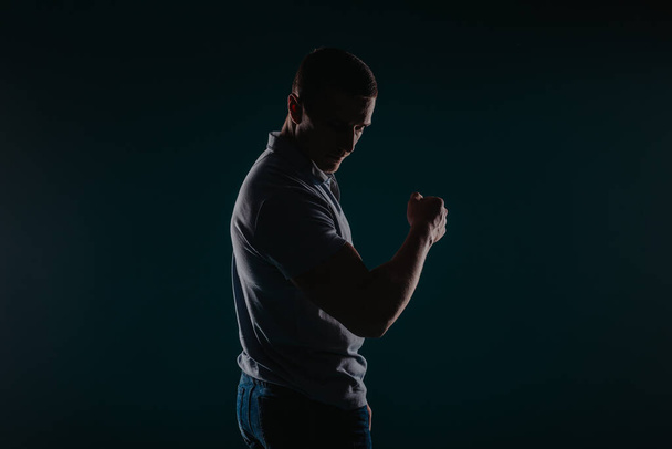 М'язистий і привабливий чоловік стоїть у темній кімнаті і згинає свій біцепс - Фото, зображення