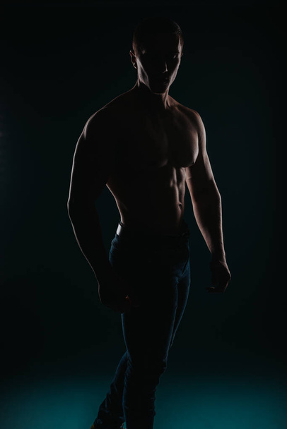 Καλοφτιαγμένος και γοητευτικός άντρας στέκεται μπροστά σε σκοτεινό φόντο και ποζάρει - Φωτογραφία, εικόνα