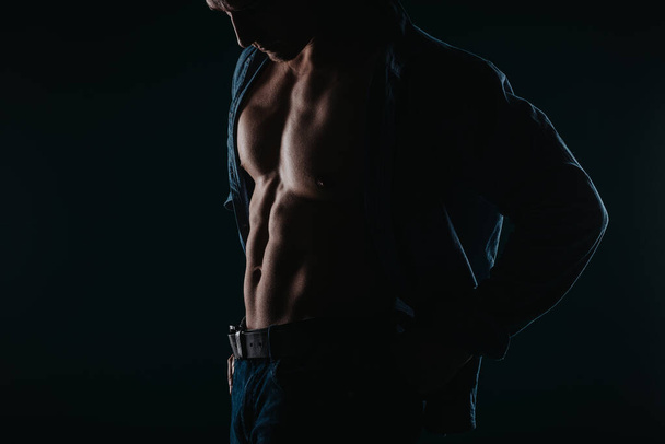 Musculoso y guapo hombre de pie en una habitación oscura y posando - Foto, Imagen