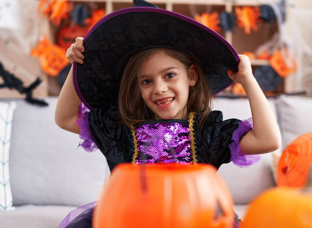 Adorable chica hispana vistiendo traje de bruja teniendo fiesta de Halloween en casa - Foto, Imagen