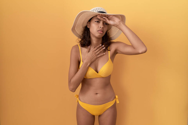 Jonge Spaanse vrouw met bikini en zomerhoed die het voorhoofd beroert tegen ziekte en koorts, griep en kou, virusziek  - Foto, afbeelding
