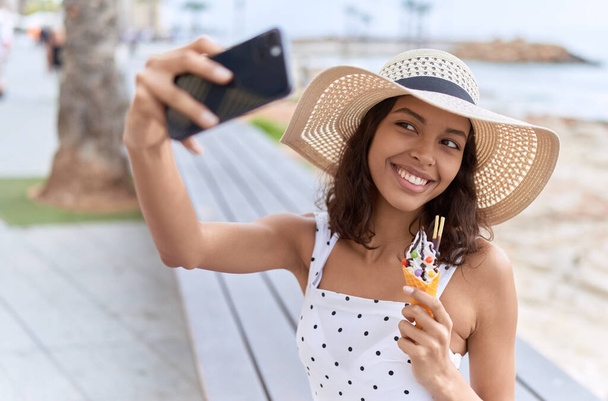 Young african american woman tourist make selfie by smartphone eating ice cream at seaside - Photo, Image
