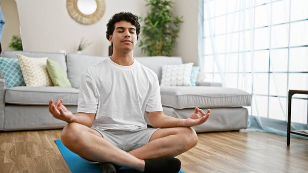 Giovane uomo latino seduto sul pavimento yoga di formazione a casa - Foto, immagini