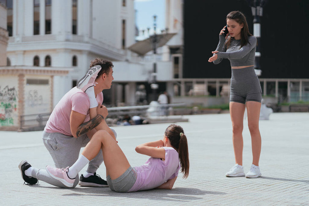Brunette sportsgirl calling an ambulance after her female friend injured her leg while training - Photo, image