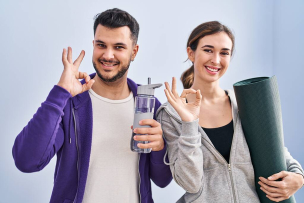 Fiatal spanyol pár visel sportruházat csinál rendben jel ujjakkal, mosolygós barátságos gesztus kiváló szimbólum  - Fotó, kép